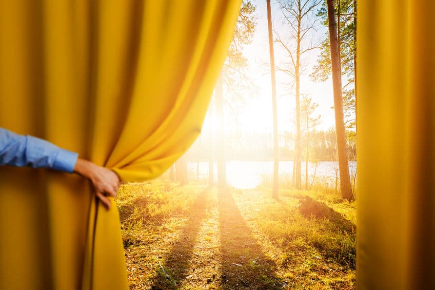 Hand opening curtain to reveal sunny landscape