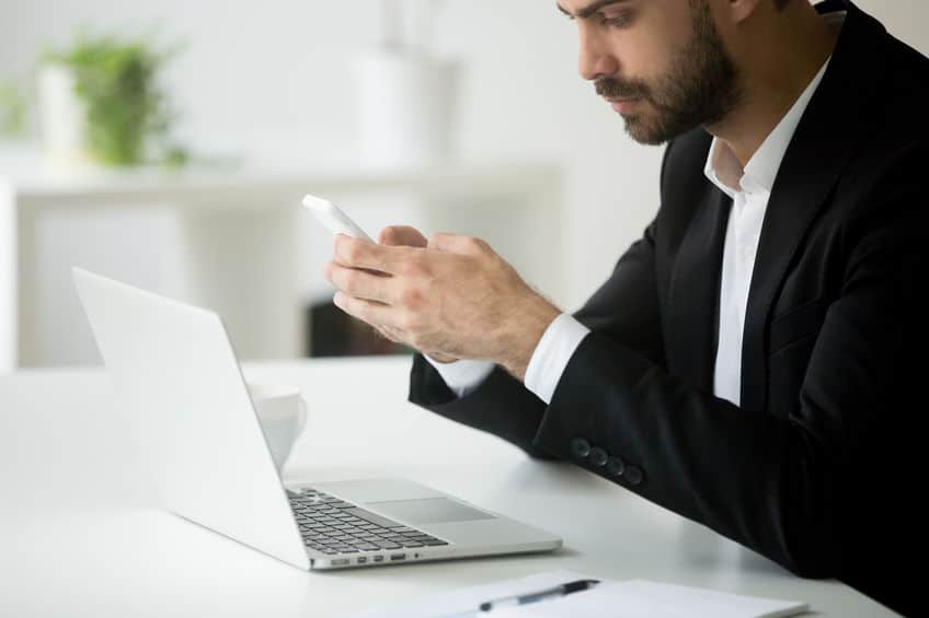 man in front of laptop looking at cell phone